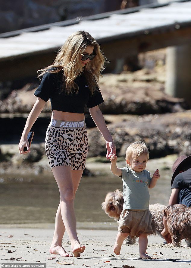 Kyle Sandilands’ wife Tegan Kynaston flaunts her toned physique in athletic attire while bringing their son Otto to a beach in Sydney.